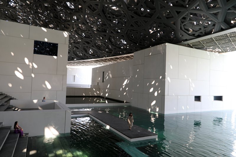 Sunlight filtering through the latticed dome over the reflecting pool at Louvre Abu Dhabi