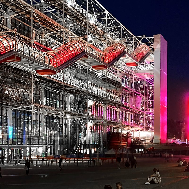 Exterior of the Centre Pompidou in Paris at night, showing its exposed structural pipes and escalator tubes