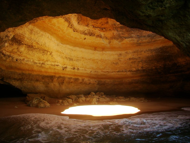 Sunlight beaming through the sea cave's rock skylight onto the sand floor at Benagil