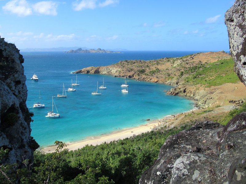 Secluded cove backed by scrub-covered hills at Colombier Beach with sailboats anchored offshore