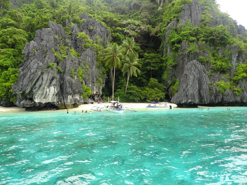 Limestone karst cliffs framing a small white-sand cove in the Bacuit Archipelago, El Nido