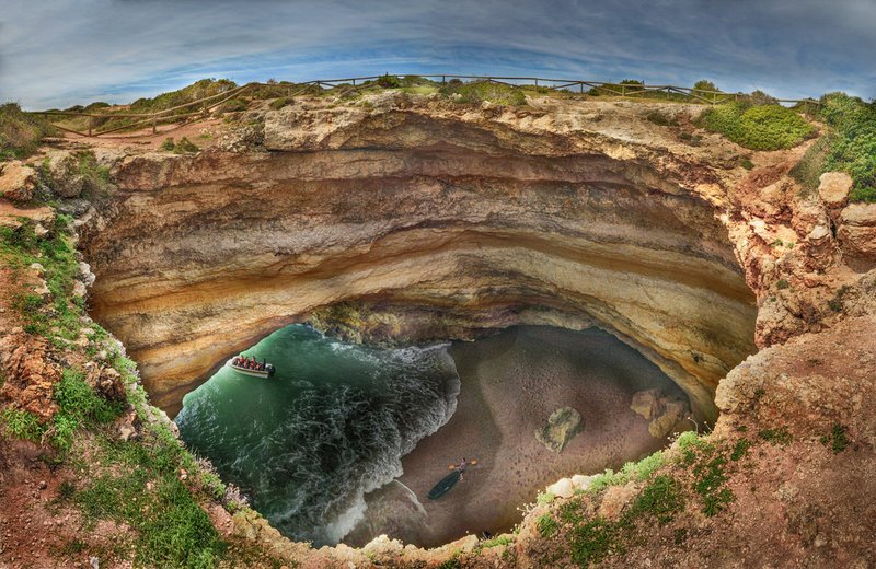 Aerial view into Benagil Cave's domed roof opening onto its sheltered beach on the Algarve coast