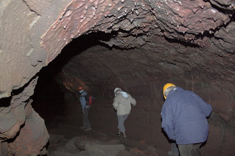 Visitors walking through the lava tube interior of Víðgelmir cave with lava drip formations overhead