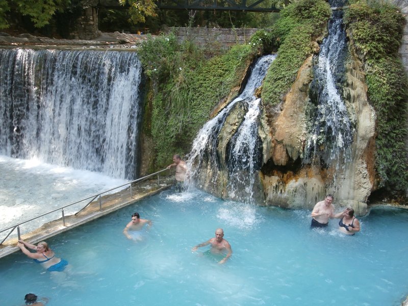 Bathers in an open-air thermal pool beneath waterfalls at Pozar