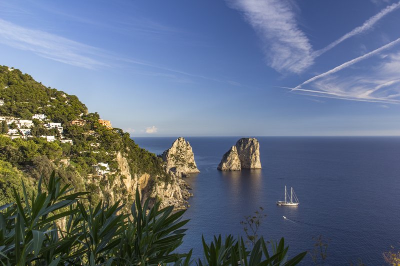 The Faraglioni rock stacks rising from the sea off Capri's coast, with a sailboat passing by
