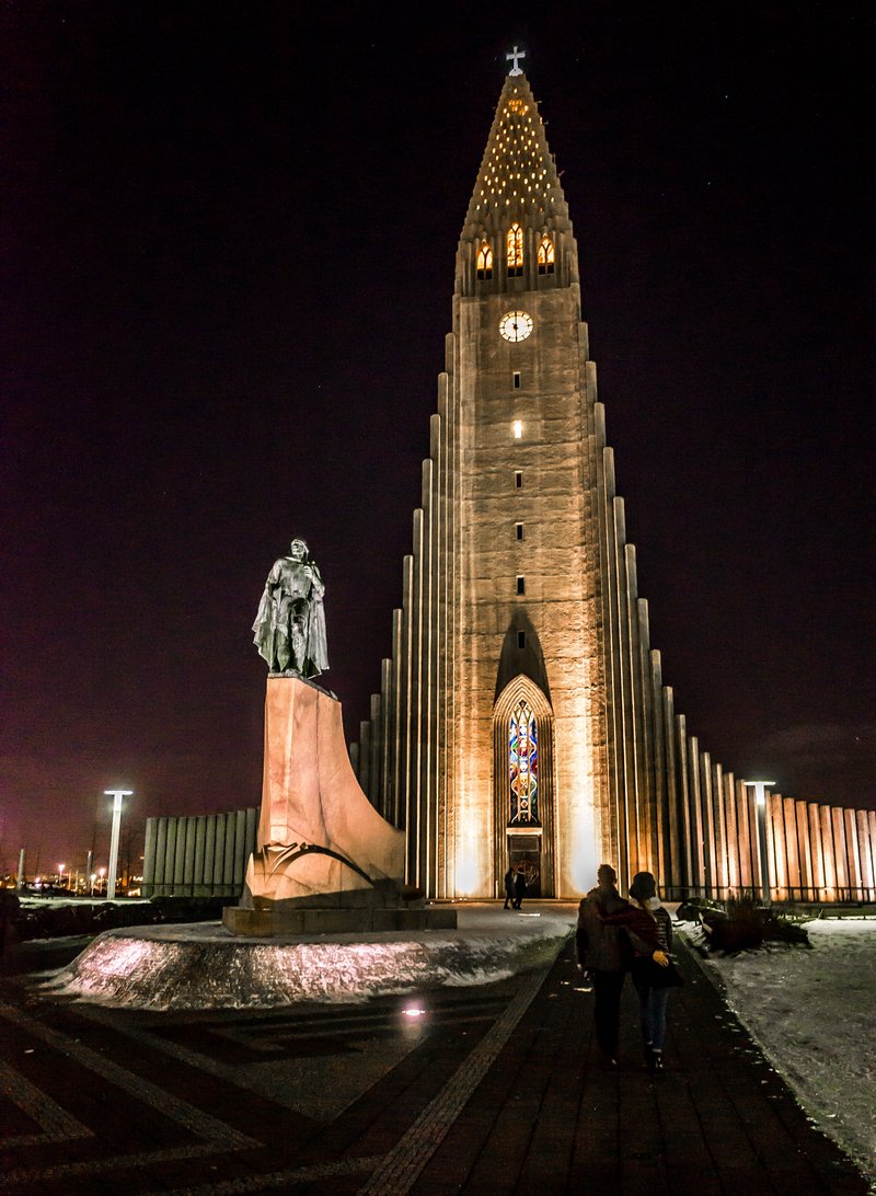 Hallgrímskirkja church tower illuminated at night, with the statue of Leif Erikson in front